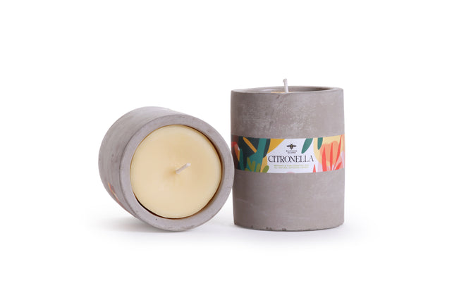 Two gray Citronella Concrete Cup Candles from Big Dipper Wax Works bring minimalist style to your space. One stands upright, showcasing a colorful label reading "Citronella Candle," making it perfect for outdoor summer evenings. The other rests on its side, revealing the yellow beeswax-soy wax blend and wick inside. Both candles are displayed against a clean white background.