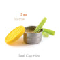 A 3 oz EcoLunchBox Seal Cup Mini stainless steel container with a yellow silicone lid, filled with dip and celery sticks, sits beside it. Text above reads "3 oz, 1/3 cup" and below, "Seal Cup Mini leak-proof mini container.