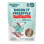 A blue and white bag of Shameless Pets Dog Treats - Bacon It Freestyle, featuring a cartoon dog in a scarf running through snowflakes, with product information highlighting digestive health benefits and bacon dog treats visible through a clear window.