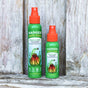 Two bottles of Badger Balm Anti-Tick Repellent Shake & Spray, a DEET-free and organic tick repellent, sit on a rustic wooden surface. The green bottles with orange spray tops display labels adorned with floral and animal designs.
