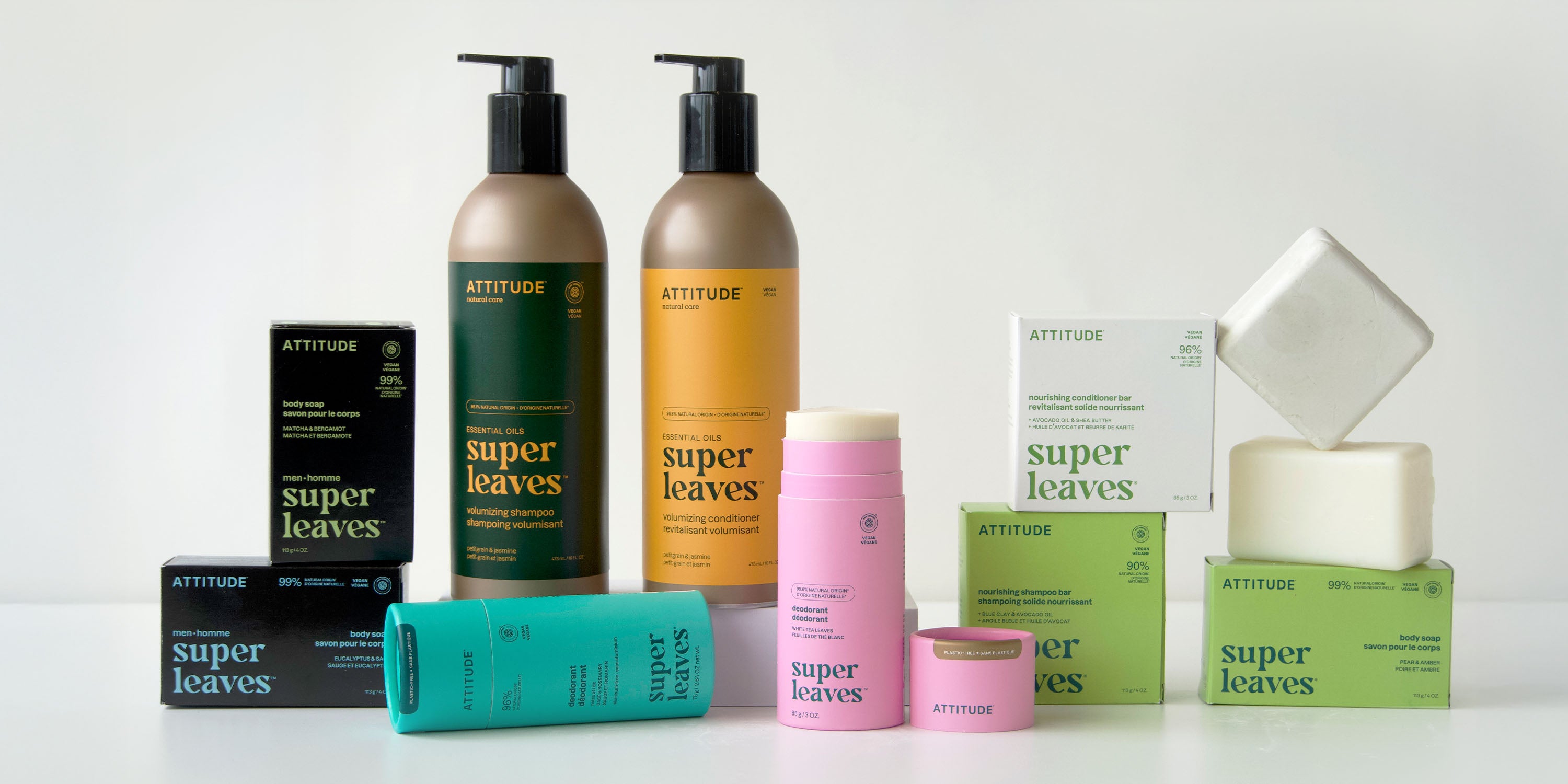 A variety of ATTITUDE Super Leaves hair and body care products, including shampoos, conditioners, deodorants, creams, and soaps, are arranged on a white surface against a light background.