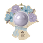 A round lavender bath bomb is packaged in a bouquet-shaped cardboard with illustrated purple and blue flowers and a blue ribbon. The label says Pacha Soap Co. Bath Bomb Card - Meadow & Air.