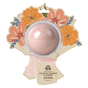 A round pink floral bath bomb from Pacha Soap Co. comes in a flower-shaped package with orange and pink blooms. The label reads “Bath Bomb Card - Orange Flower & Amber.”.