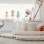 A tray on a kitchen countertop near a window holds Full Circle Beachy Clean Coconut Scour Pads, a soap dispenser, and a loofah. The organized scene is bright with natural light and neutral tones.