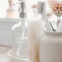 A close-up of Full Circle's Beachy Clean Coconut Scour Pads, alongside a glass soap dispenser and natural sponge, all displayed on a white surface in soft natural light.