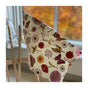 A pack of Bee's Wrap Reusable Beeswax Food Wraps – Assorted 3 Pack is draped over a wooden chair by a window, highlighting sustainable food storage as autumn foliage glows outside.