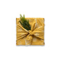 A present wrapped in Bee's Wrap Reusable Gift Wrap Set—certified organic cotton with a white honeycomb pattern—tied in a knot atop and adorned with pine sprigs, sits centered against a white background.