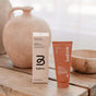 A tube and box of before Sensitive Purifying Toothpaste w/ Fluoride, Anti-Cavity are shown on a wooden surface, with blurred ceramic vases in the background.