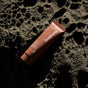 A brown tube of before Sensitive Purifying Toothpaste w/ Fluoride, Anti-Cavity sits on a textured rock surface under natural sunlight, casting shadows and accentuating the earthy hues of both the toothpaste and the rock.