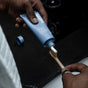 Someone squeezes before Whitening Purifying Toothpaste w/ Fluoride, Anti-Cavity from a blue tube onto a bamboo toothbrush above a dark bathroom sink.
