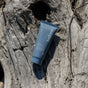 A dark blue tube of before Whitening Purifying Toothpaste w/ Fluoride, Anti-Cavity rests on weathered driftwood outdoors, with sunlight and shadows accentuating the woods textured surface.