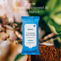 A pack of Biom Full Body Wipe Go-Pack sits inside a halved coconut, with blurred coconut and green leaves in the background. Text above reads: Smells like: Bergamot, coconut & shea butter. Formulated with skin-safe ingredients, these body wipes leave you feeling refreshed and clean anytime, anywhere.