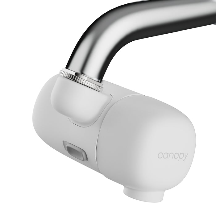 A close-up of a white Canopy Faucet Filter attached to a curved silver faucet. The modern filter showcases a visible button, the Canopy brand name, and provides filtered water with effective chlorine reduction.