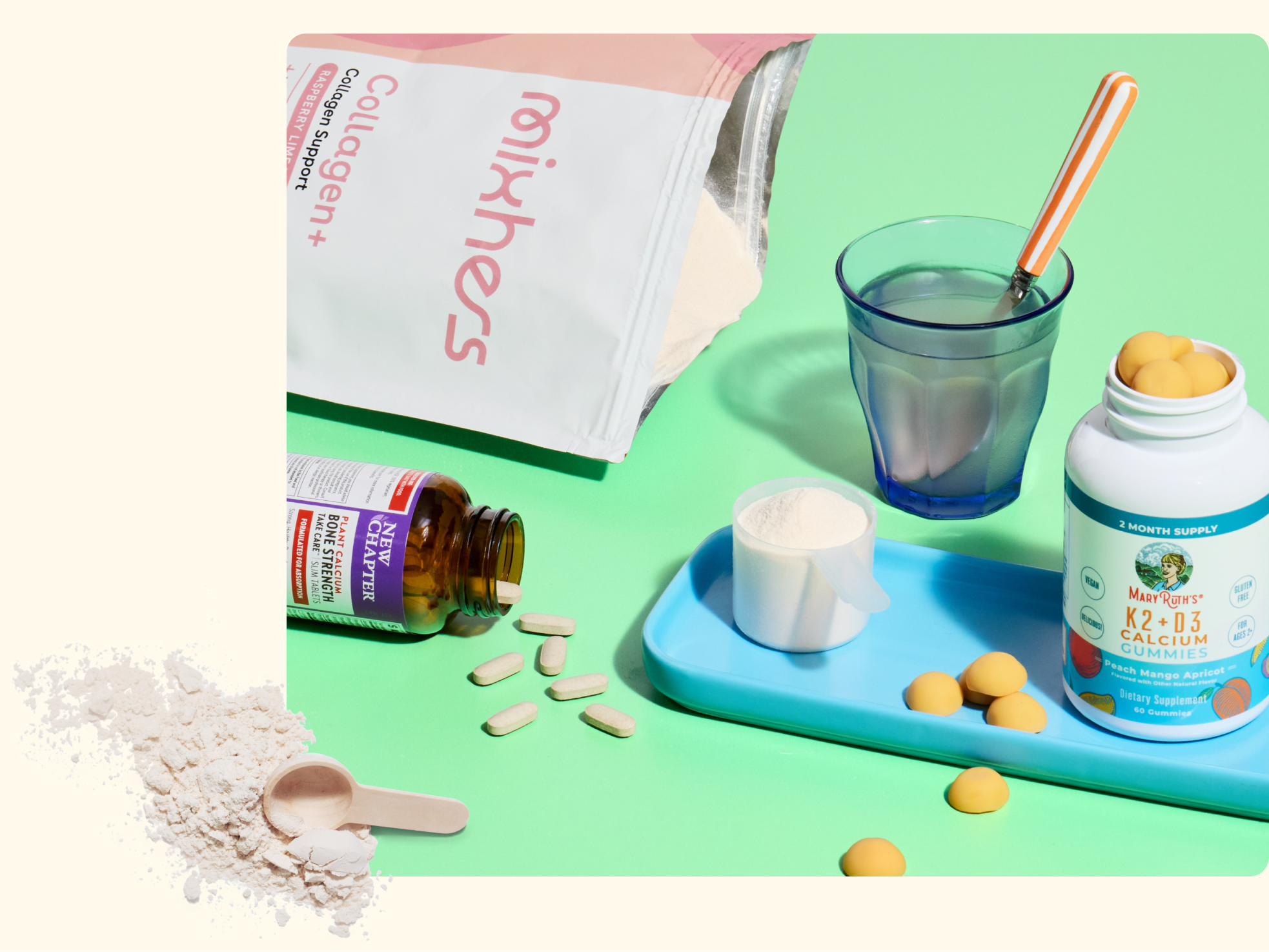 A packet of collagen powder, a bottle of multivitamins, a bottle of calcium gummies, a glass of water with a striped straw, several tablets, a scoop of powder, and scattered gummies on a green surface.