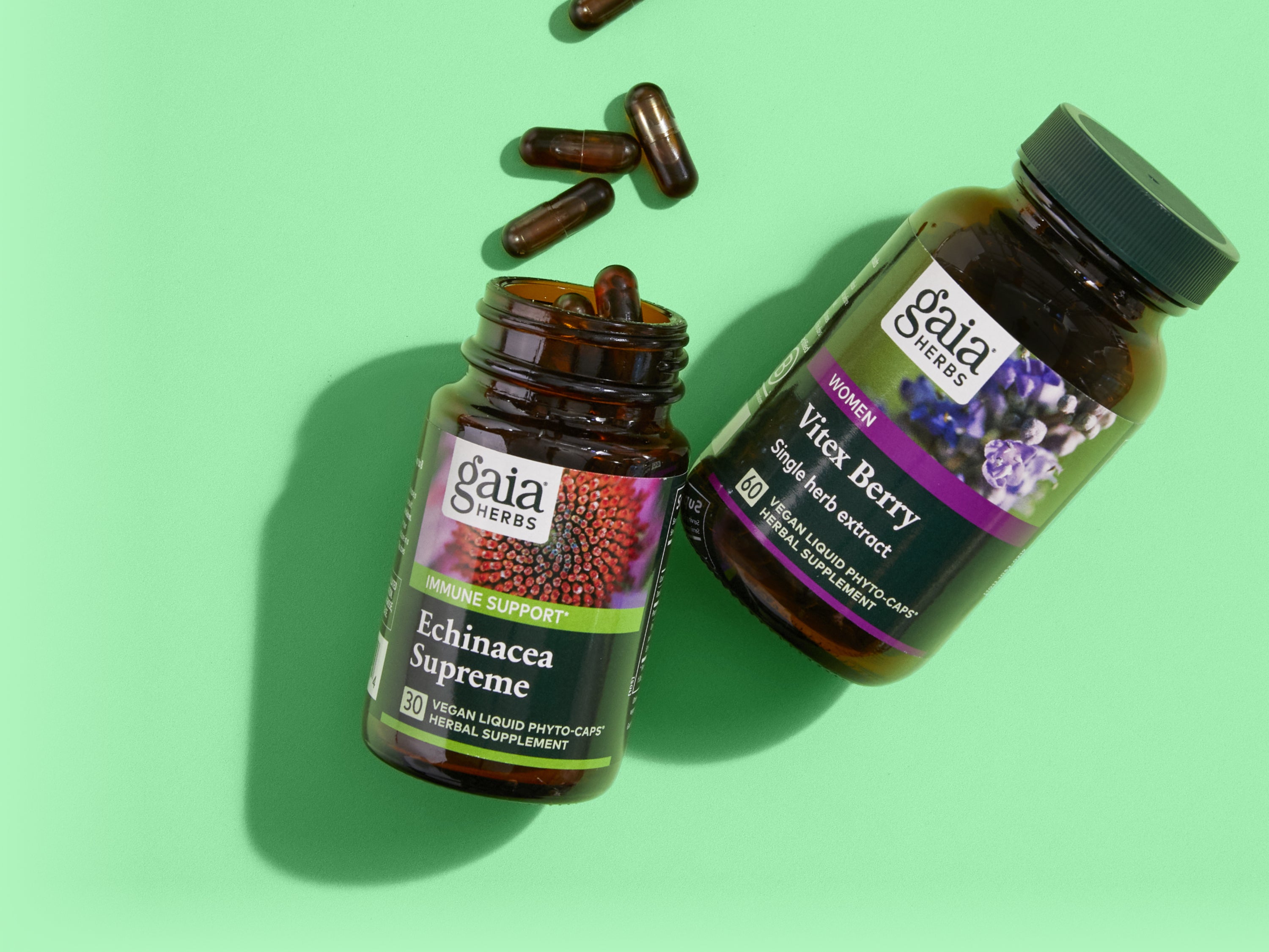 Two Gaia Herbs supplement bottles on a light green surface, one labeled Echinacea Supreme with capsules spilling out, and the other labeled Vitex Berry. Three loose capsules are also visible.