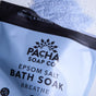 A partially open bag of Pacha Soap Co. Breathe Salt Soak rests on a surface, with light blue Epsom salt and the calming aroma of eucalyptus oil spilling out above the package.