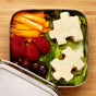 The EcoLunchBox Solo Cube - Stainless Steel Sandwich Container holds lettuce, puzzle-shaped sandwiches, orange bell pepper slices, strawberries, and grapes, all arranged neatly on a wooden surface.