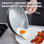 A hand slides a sunny-side-up egg from a GreenPan Chatham Open Frypan, 10 in, onto a plate with bacon. Text: PFAS-free ceramic nonstick cookware, reinforced with diamonds.