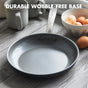 The GreenPan Chatham Open Frypan, 12 in, PFAS free with a hard anodized body and metal handle, sits on a wooden table next to a white bowl of eggs and mugs. Text above reads: DURABLE WOBBLE-FREE BASE.