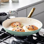 Three blueberry pancakes cook in a GreenPan Reserve Ceramic Nonstick frying pan (part of the 10-Piece Cookware Set) on a gas stove, with a bowl of blackberries and syrup nearby. The PFAS-free cookware from GreenPan ensures safe, easy flipping every time.