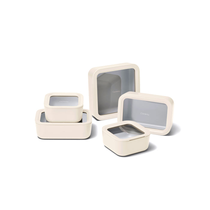 The Caraway 13 Piece Glass Food Storage Set features cream-colored, rectangular and square containers with ceramic coating and transparent lids, shown nested together on a white background.