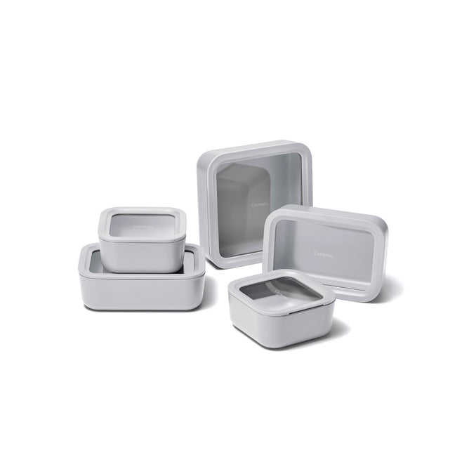 The Caraway 13 Piece Glass Food Storage Set is displayed on a white surface, with some pieces stacked and others separated, highlighting the versatility and different sizes of these stylish containers.