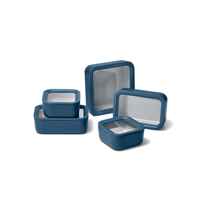 The Caraway 13 Piece Glass Food Storage Set features blue containers with transparent lids, arranged on a white background, stacked and standing. These non-toxic glass containers keep your food fresh and organized.