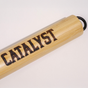 A light wooden cylinder with CATALYST in bold black letters and a black metal loop on one end, shown on white—ideal for use with the Catalyst Pet Wide Slatted Litter Scoop.