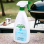 A bottle of Charlie's Soap Indoor & Outdoor Multi-Purpose Surface Cleaner Spray sits on an outdoor table near a grill, with greenery blurred in the background.