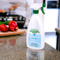 A bottle of Charlie's Soap Indoor & Outdoor Multi-Purpose Surface Cleaner Spray sits on a kitchen countertop, with vegetables and a cutting board visible in the blurred background.