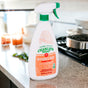 A bottle of Charlie's Soap Kitchen & Bath Household Surface Cleaner sits on a kitchen counter near a stovetop, with blurred kitchen items in the background.