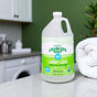 A large bottle of Charlie's Soap Liquid Laundry Detergent - Ultra Concentrated sits on a countertop next to a folded white towel, with a green wall and kitchen cabinets behind it, showcasing its residue-free laundry results.