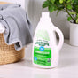 A bottle of Charlie's Soap Liquid Laundry Detergent - Ultra Concentrated sits on a white surface next to a woven basket of gray towels, with a green plant in the background.