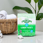 A bag of Charlie's Soap Powder Laundry Pods - Ultra Concentrated sits on a counter beside a wicker basket of white towels and a green plant, with one white pre-measured detergent pod displayed in front.