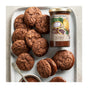 A plate of chocolate cookies sits beside a jar of Savannah Bee Company Whipped Honey with Chocolate and a bowl of spread, with some cookies made into sandwiches.