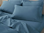 A neatly made bed featuring Coyuchi’s Classic Organic Sateen Sheet Set in blue, including GOTS certified organic cotton sheets and pillowcases, topped with a matching blanket. The bedding looks smooth and clean, creating a cozy and inviting atmosphere.