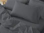 A neatly made bed with Coyuchi’s Classic Organic Sateen Sheet Set in dark gray, featuring GOTS certified organic cotton sheets, pillowcases, and a comforter, sits next to a light wooden bedside table.