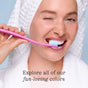 A smiling person in a white bathrobe and towel turban brushes their teeth with a pink COCOLAB Cocobrush Toothbrush, winking playfully. Text reads: Explore all of our fun-loving colors.