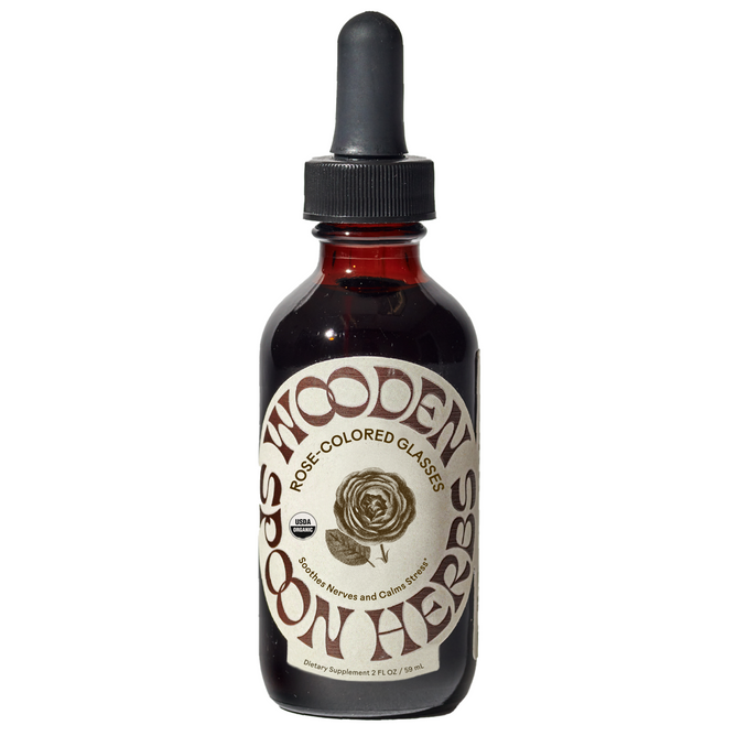 A brown glass dropper bottle labeled Wooden Spoon Herbs Rose-Colored Glasses Tincture, with a rose illustration, contains a mood-boosting dietary supplement for stress support.