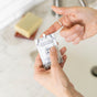 Someone squeezes Little Seed Farm's Goat's Milk Moisturizer - Sample for sensitive skin from a small packet onto their finger, with a bar of soap and sink in the background.
