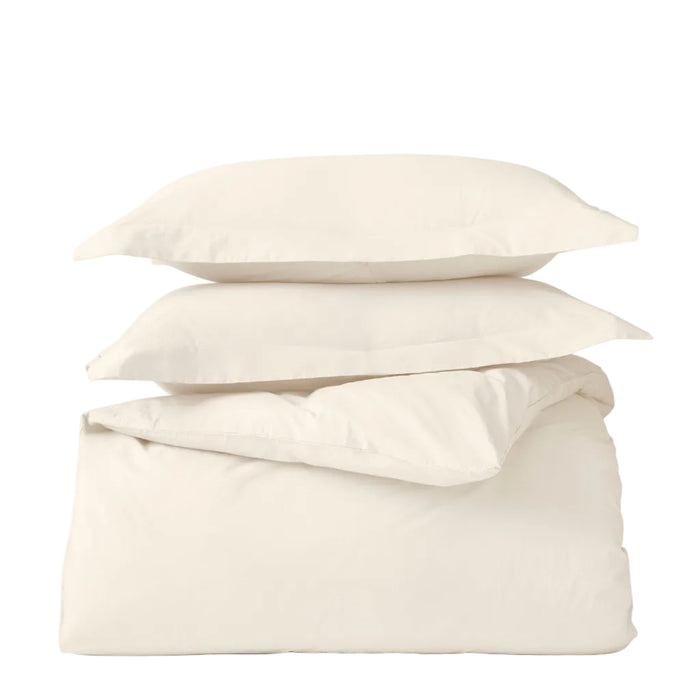 Two cream-colored pillows are stacked on a folded Coyuchi Classic Organic Sateen Duvet Set, all GOTS certified and shown against a plain white background.