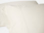 Two cream-colored Classic Organic Sateen Pillowcases by Coyuchi, king size with subtle seam detail, shown close up against a white background.