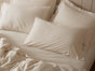 A neatly made bed features two Coyuchi Classic Organic Sateen Pillowcases at the head, complemented by organic cotton sateen sheets and a wrinkle-resistant blanket, all set against a light-colored wall.