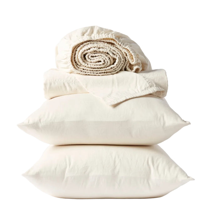 Two cream-colored pillows stacked with a folded flat sheet and rolled-up fitted sheet from the Coyuchi Classic Organic Sateen Sheet Set, all GOTS certified organic cotton, neatly arranged against a white background.
