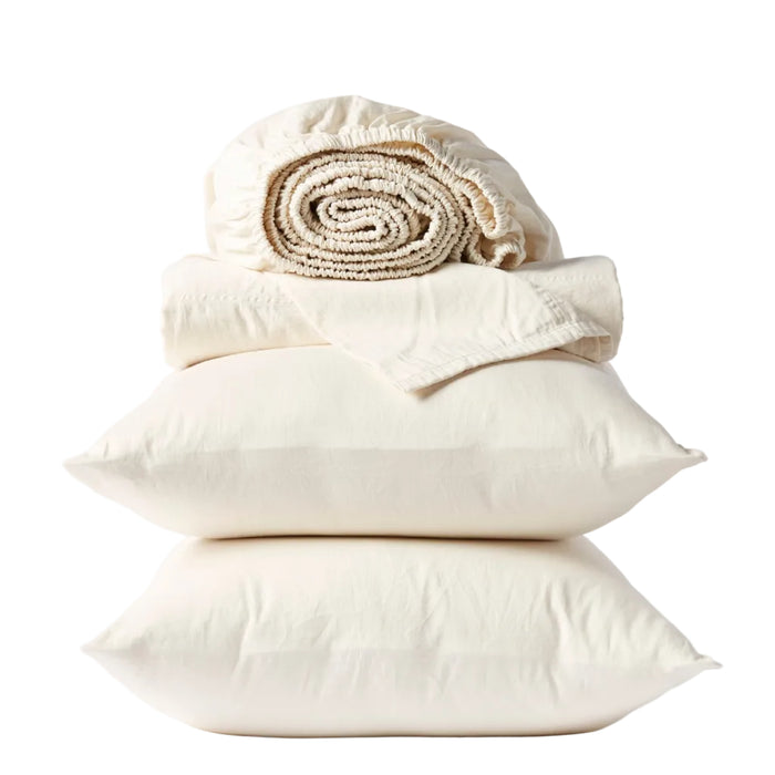 Two cream-colored pillows stacked with a folded flat sheet and rolled-up fitted sheet from the Coyuchi Classic Organic Sateen Sheet Set, all GOTS certified organic cotton, neatly arranged against a white background.