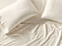 Overhead view of a bed with two cream-colored pillows and the Coyuchi Classic Organic Sateen Sheet Set, featuring soft, slightly wrinkled bedding that looks inviting and ready for use.