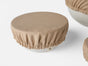A Coyuchi Conserve Organic Bowl Cover in beige with an elastic edge fits snugly over a white bowl on a white surface, while another covered bowl appears in the background—an eco-friendly, zero-waste kitchen essential.