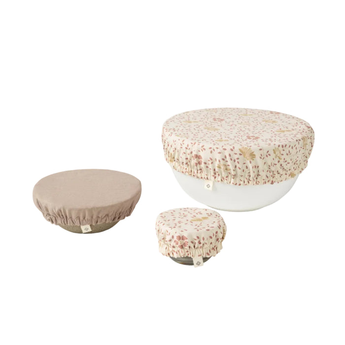 Three bowls of different sizes are covered with Coyuchi's Conserve Organic Bowl Covers in beige and floral patterns—reusable, eco-friendly covers perfect for a zero-waste kitchen. The set is displayed on a light background.
