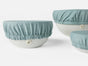 Three white bowls are topped with Coyuchi's Conserve Organic Bowl Covers in light blue. These reusable covers have elastic edges for a snug fit—ideal for a zero-waste kitchen and keeping food fresh.