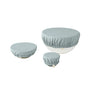 Three white bowls of varying sizes are topped with Coyuchi Conserve Organic Bowl Covers in light blue—reusable, organic cotton covers ideal for a zero-waste kitchen—displayed on a plain white background.